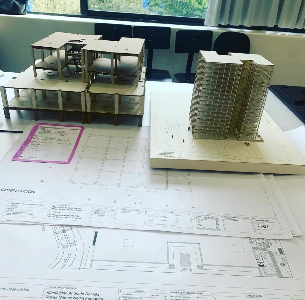 Maqueta estructural abierta junto al modelo de la torre médica, sobre las láminas de cimentación